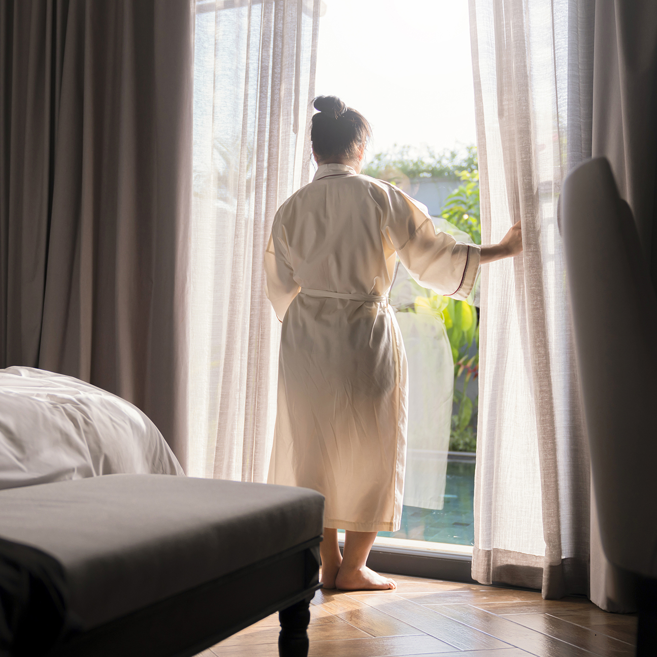 Young asian female woman stand open white curtains sheer at the window, the morning after waking up in the bedroom hotel. Woman wake up with a fresh and open the curtains on the windows.